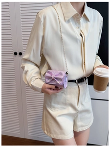 Detail of a purple iridescent mini bag with a bow and gold chain strap