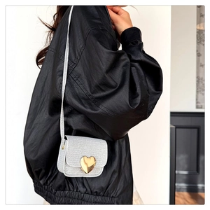 Détail d'un mini sac argenté à paillettes avec boucle coeur dorée porté en bandoulière
