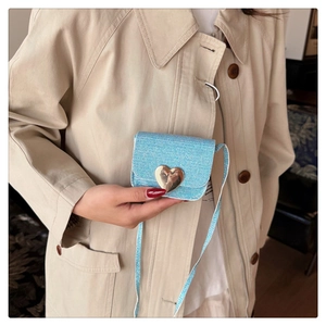 Détail du mini sac en tweed bleu clair avec fermoir coeur doré porté par un mannequin