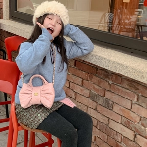 Girl's pink quilted bow handbag with gold chain strap shown in a lifestyle street setting