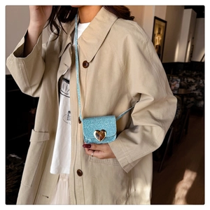 Gros plan d'un mini sac bleu pailleté avec fermoir cœur porté sur un manteau beige