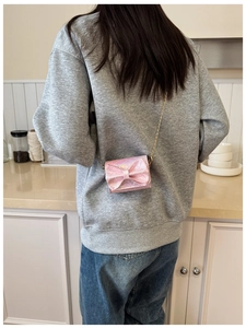Close-up of pink quilted mini crossbody bag with large bow and gold chain strap