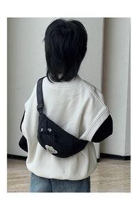 Vue arrière d'un enfant portant un sac de poitrine noir avec un écusson planète verte