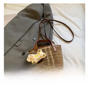 Close-up of brown plaid tweed crossbody bag with leather handle and cute lamb pendant detail