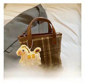 Detail of checkered plaid handbag with a plush horse charm and brown leather handle