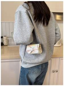 Iridescent mini crossbody bag with bow and gold chain strap shown on a young girl