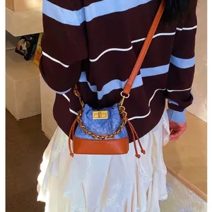 Mini sac seau matelassé en denim bleu et cuir marron avec chaîne dorée et fermoir