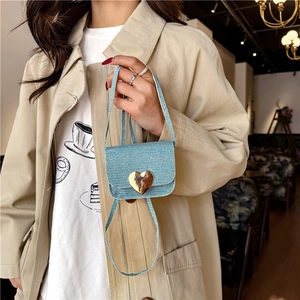 Mini sac à bandoulière bleu clair avec cœur doré tenu par un mannequin en trench beige