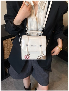 Detail of cream leather crossbody bag with ladybug patch and logo on black suit