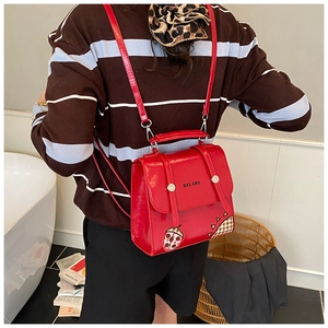 Detail of red leather backpack with ladybug patch and metallic clasp on flip cover