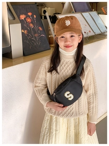 Close-up of a black kids' crossbody bag with white 'S' patch worn by a child in a cafe