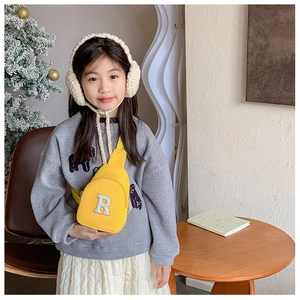 Détail d'un enfant portant un sac de poitrine jaune avec un patch lettre R en peluche blanche