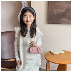 Pink cylindrical mini tote bag for kids held by a child model in a warm room setting
