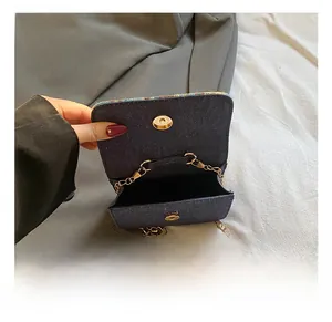 Detail of dark blue denim mini bag showing gold chain strap and magnetic snap closure