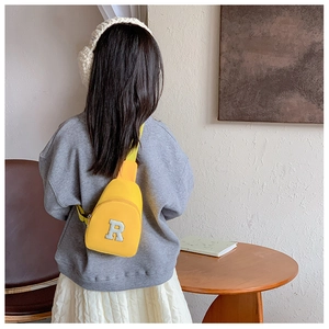 Détail d'un sac de poitrine jaune pour enfant avec écusson lettre R en peluche blanche