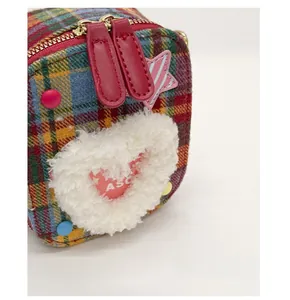 Détail du sac à carreaux avec cœur en peluche blanche, patch étoile et zip en cuir rouge