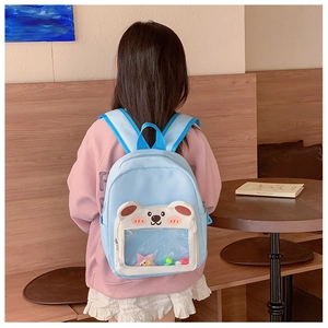 Detail of light blue backpack with transparent bear-shaped window and colorful pom poms