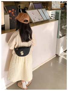 Close-up of kids black chest bag with yellow 3D letter S on beige knit sweater