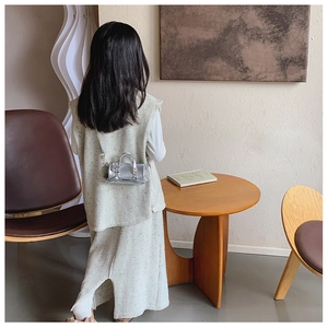 Mini silver metallic cylinder bag shown with shoulder strap on a knit dress model