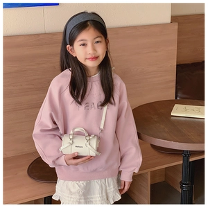 Close-up of a white cylindrical mini crossbody bag with top handles on a child model