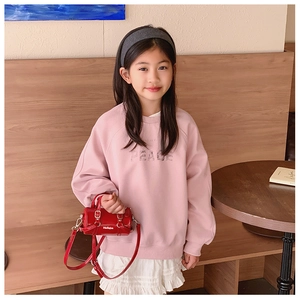 Close-up of a small red cylinder bag for kids paired with a pink PEACE sweatshirt