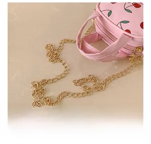 Detailed close-up of the gold metal chain and cherry print on this pink mini bag