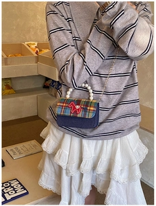 Detail of kids plaid handbag with pearl handle and red horse patch on denim fabric