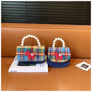 Detail of checkered mini kids handbag featuring a blue denim body and white pearl handle