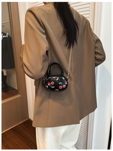 Close-up of mini cherry print bag with gold chain strap on a brown blazer outfit