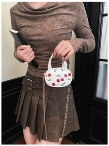 Close-up of a white mini crossbody bag with cherry prints and a golden chain strap