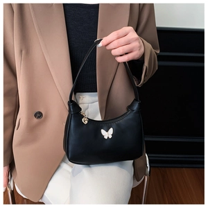 Détail d'un sac à main demi-lune noir avec papillon blanc et pendentif cœur doré élégant
