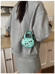 Detail of mint green cherry print mini bag with gold chain strap on a grey hoodie