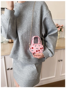 Mini pink crossbody bag with cherry prints and gold chain shown in a lifestyle setting