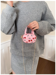 Close-up of pink mini crossbody bag with cherry patterns and golden chain strap