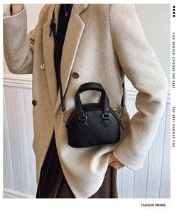 Detail of black litchi pattern mini shell bag held by model with adjustable shoulder strap
