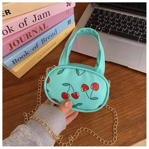 Close-up of mint green cherry mini bag featuring a gold chain strap on a wooden desk