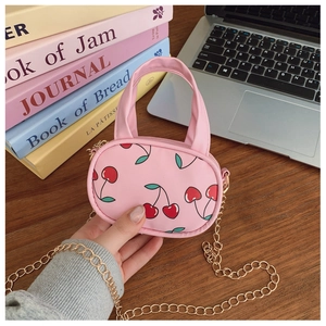 Macro view of mini pink crossbody bag with red cherry prints and golden chain strap