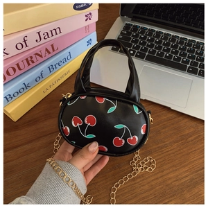 Close-up of kids' black cherry print crossbody bag with gold chain strap on table