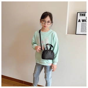 Detailed view of mini black pebble leather shell bag worn by a young girl in a room