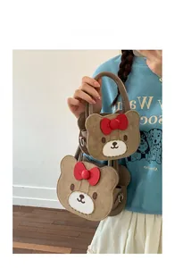Detail of brown cartoon bear handbag with red bow showing smooth suede texture and top handle