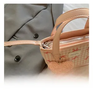 Détail de la texture à carreaux roses, nœud rouge et breloque coeur en peluche sur le sac