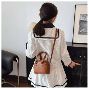 Rear view of a child carrying the brown shell-shaped crossbody bag with adjustable strap