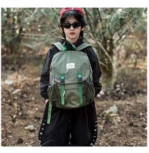 Close-up of green checkered hiking backpack for kids with Mountains patch in nature