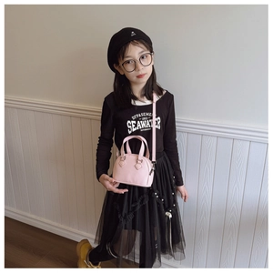 Pink mini shell bag for kids with litchi texture and adjustable shoulder strap worn by model