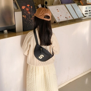 Kids black nylon chest bag with varsity S patch shown in a cozy cafe setting