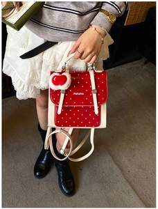 Polka dot backpack detail with plush heart charm and Helahe logo displayed by a model