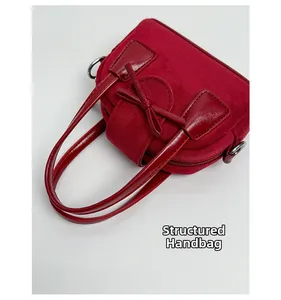Detalle del bolso de ante rojo con asa estructurada y adorno de lazo decorativo