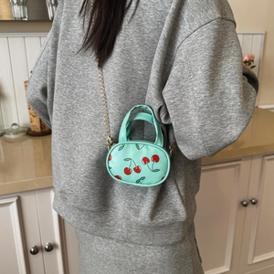 Mint green cherry print mini bag for kids with gold chain strap shown on model
