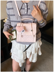 Detail shot of a pink polka dot handbag with a heart-shaped plush keychain and branded text