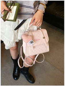Pink polka dot backpack with plush heart charm shown in a stylish lifestyle setting
